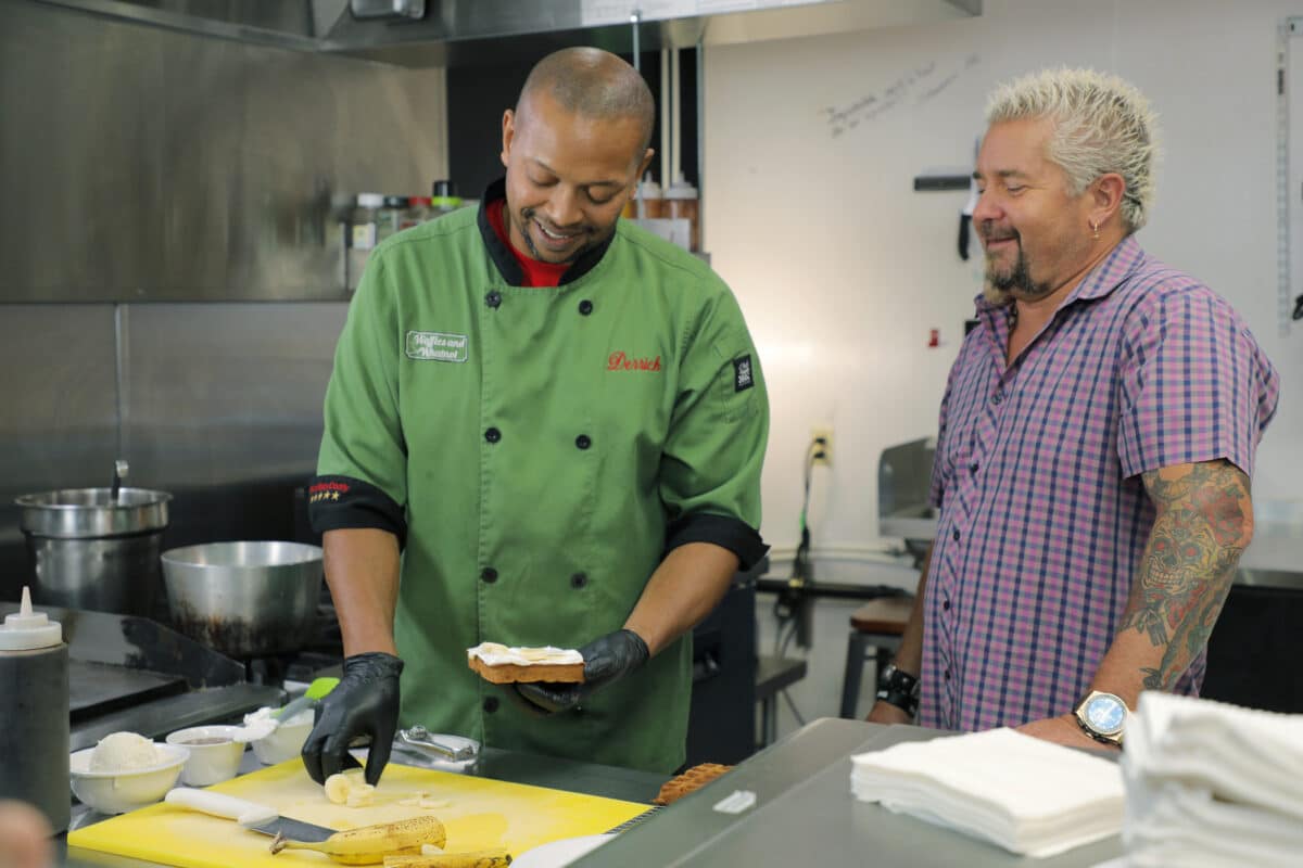 Host Guy Fieri and owner Derrick Green preparing food in the kitchen of Waffles and Whatnot in Anchorage, AK, as seen on Diners, Drive-ins and Dives, season 35.