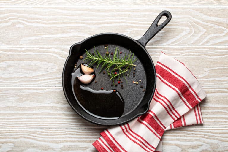 Black cast iron frying pan with rosemary, garlic, pepper, oil